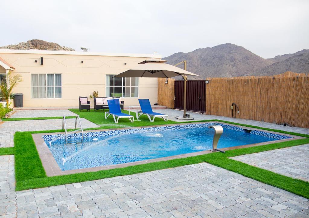 - une piscine avec des chaises et un parasol dans la cour dans l'établissement 800 Mountain Resort Vacation House, à Fujaïrah