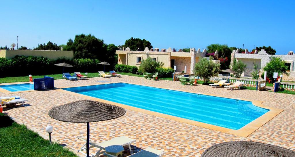 Kaouki beach Apart'hotel في سيدي كاوكي: مسبح مع كراسي ومظلات بجوار منزل