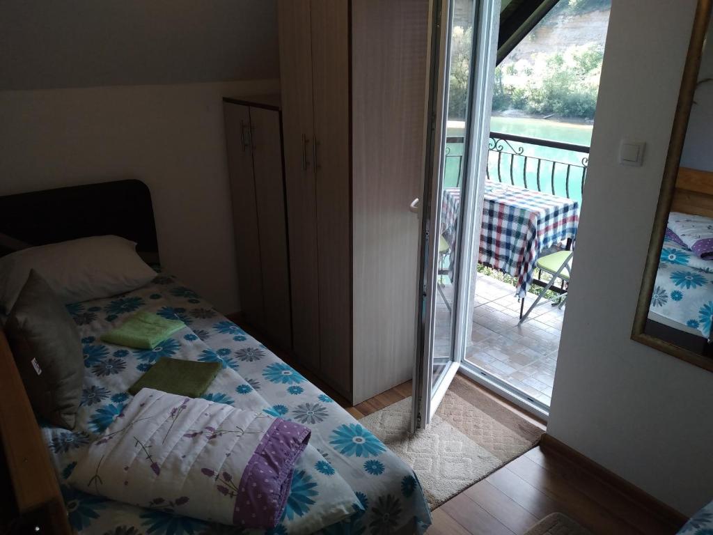 a bedroom with a bed and a balcony with a table at Vikendica pored Drine Foča in Handići