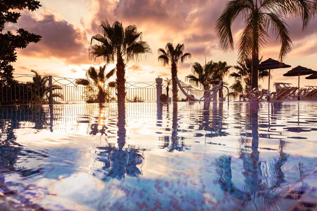 a swimming pool with palm trees and a sunset at Residence Porto Ulisse in Parghelia