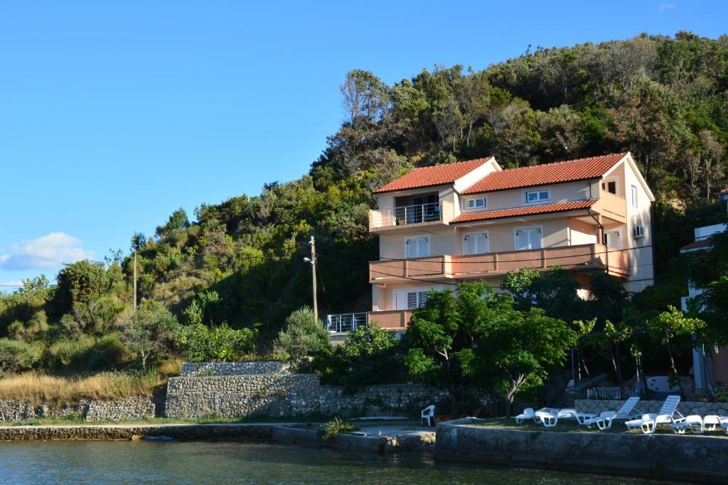 a house on a hill next to a body of water at Apartments by the sea Supetarska Draga - Donja, Rab - 17201 in Rab