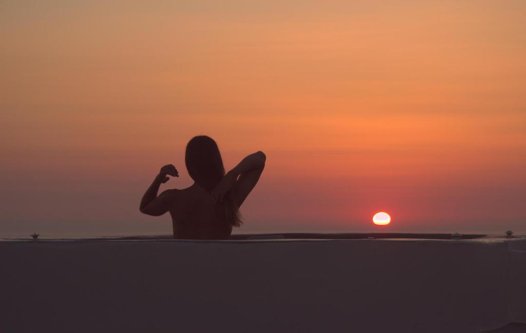 une femme assise sur la plage pour admirer le coucher du soleil dans l'établissement Sando Traditional Cave Villas with Jacuzzi and Sea view, à Vourvoúlos