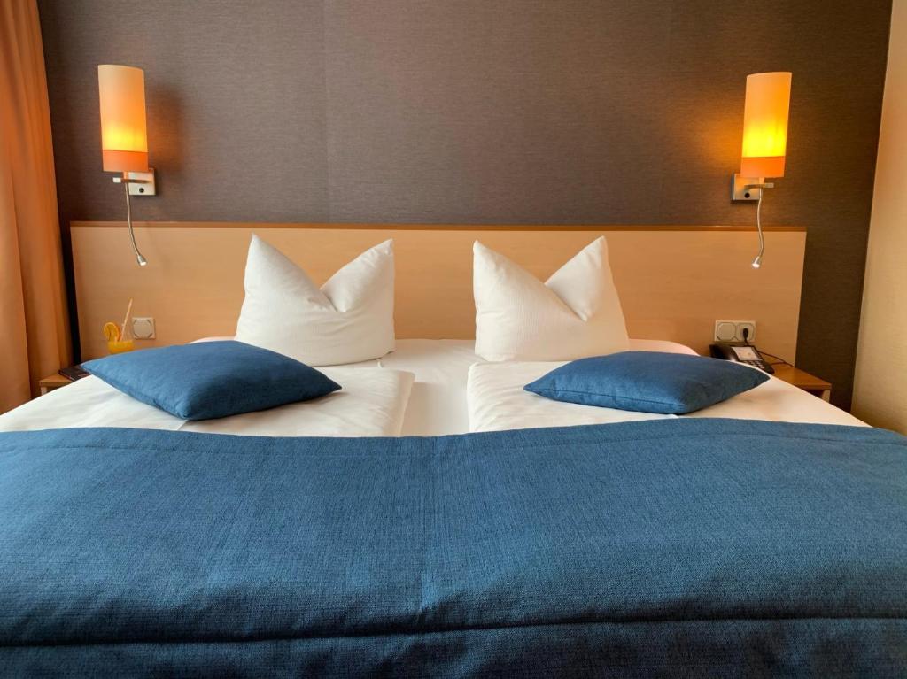 ein großes Bett mit zwei blauen Kissen darauf in der Unterkunft Atrium Hotel Krüger in Rostock