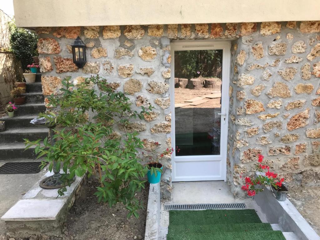 une maison en pierre avec une porte blanche et quelques plantes dans l'établissement Studios de l'Etang du perray, à Le Perray-en-Yvelines