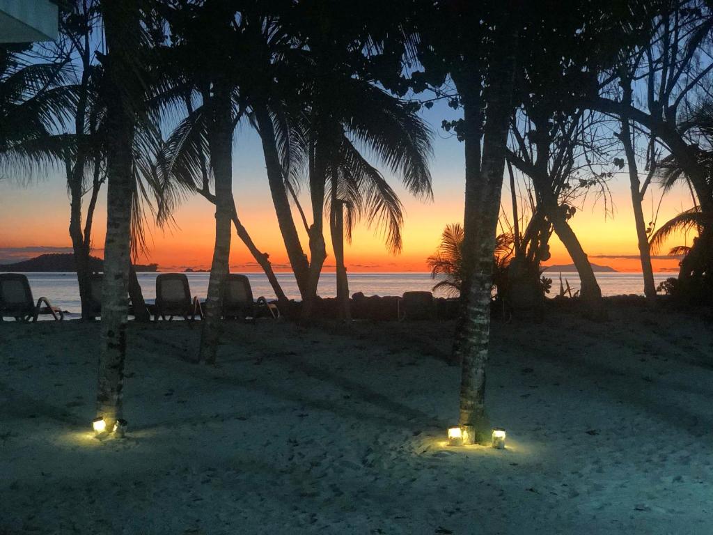una puesta de sol en una playa con palmeras y luces en Cap Jean Marie Beach Villas, en Anse Kerlan