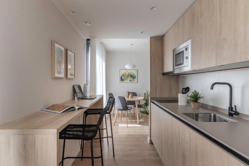 a kitchen with a sink and a counter with chairs at Apartamentos Líbere Pamplona Yamaguchi in Pamplona