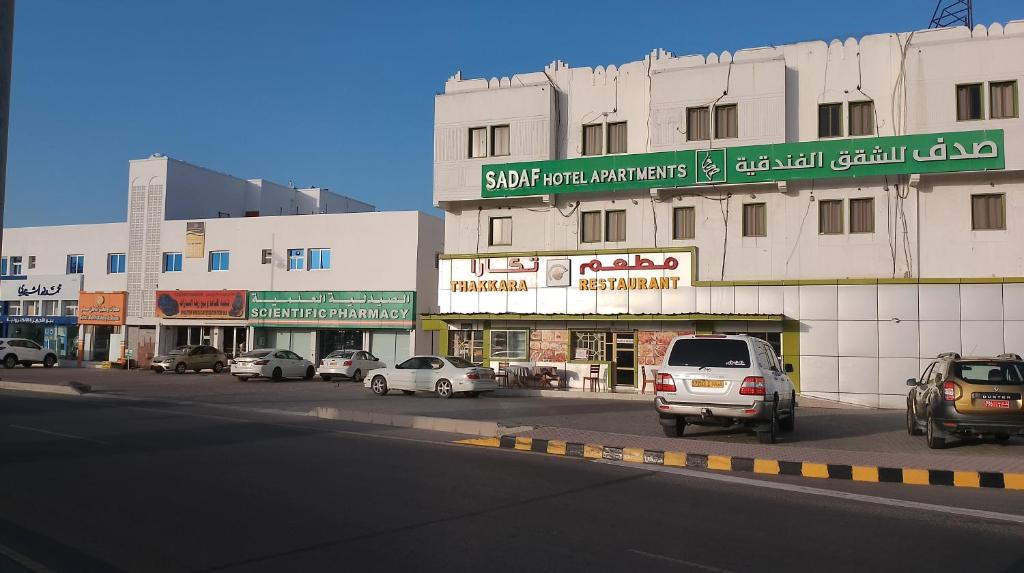 蘇哈爾的住宿－Sadaf Hotel Apartments，一条城市街道,汽车停在建筑前