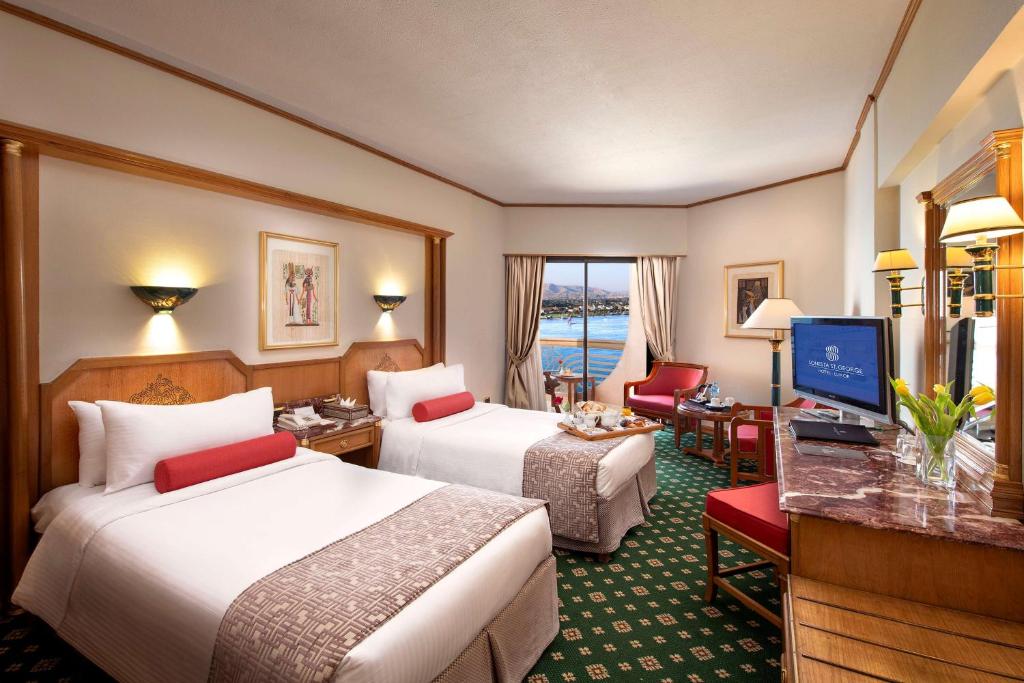 a hotel room with two beds and a desk at Sonesta St. George Hotel - Convention Center in Luxor