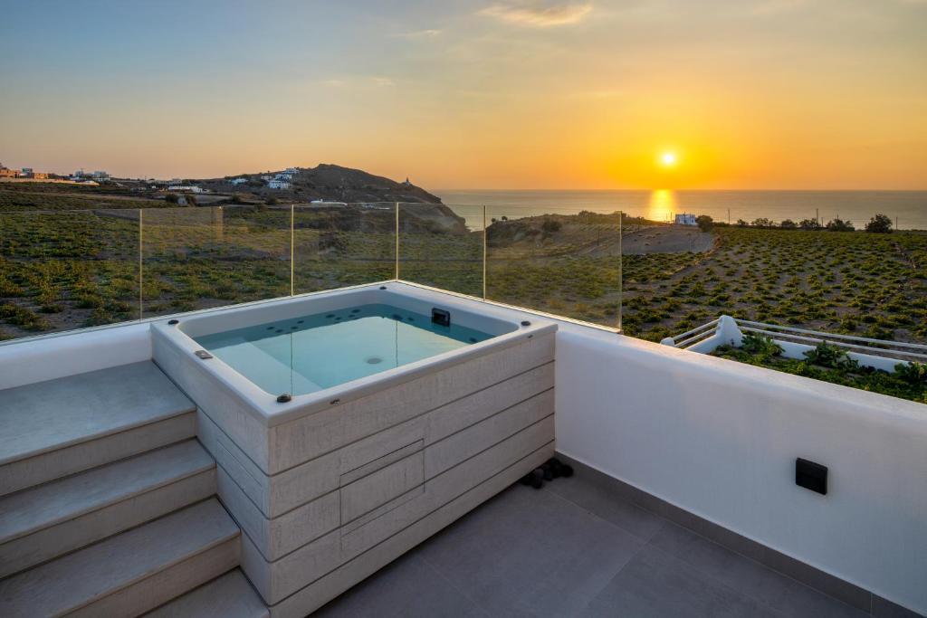 La Ponta Villas & Suites في أكروتيري: حوض استحمام ساخن على شرفة المنزل مع غروب الشمس