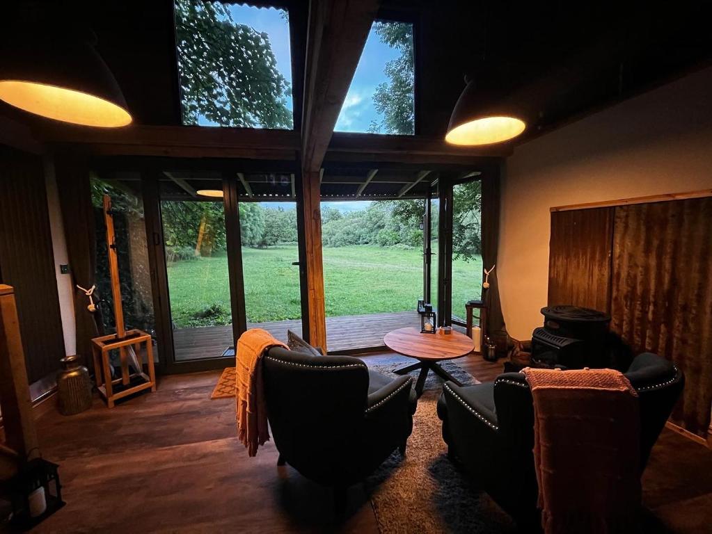ein Wohnzimmer mit Stühlen, einem Tisch und einem großen Fenster in der Unterkunft Lynbrook Haybarn, Hot tub and outdoor kitchen, New Forest in Ringwood
