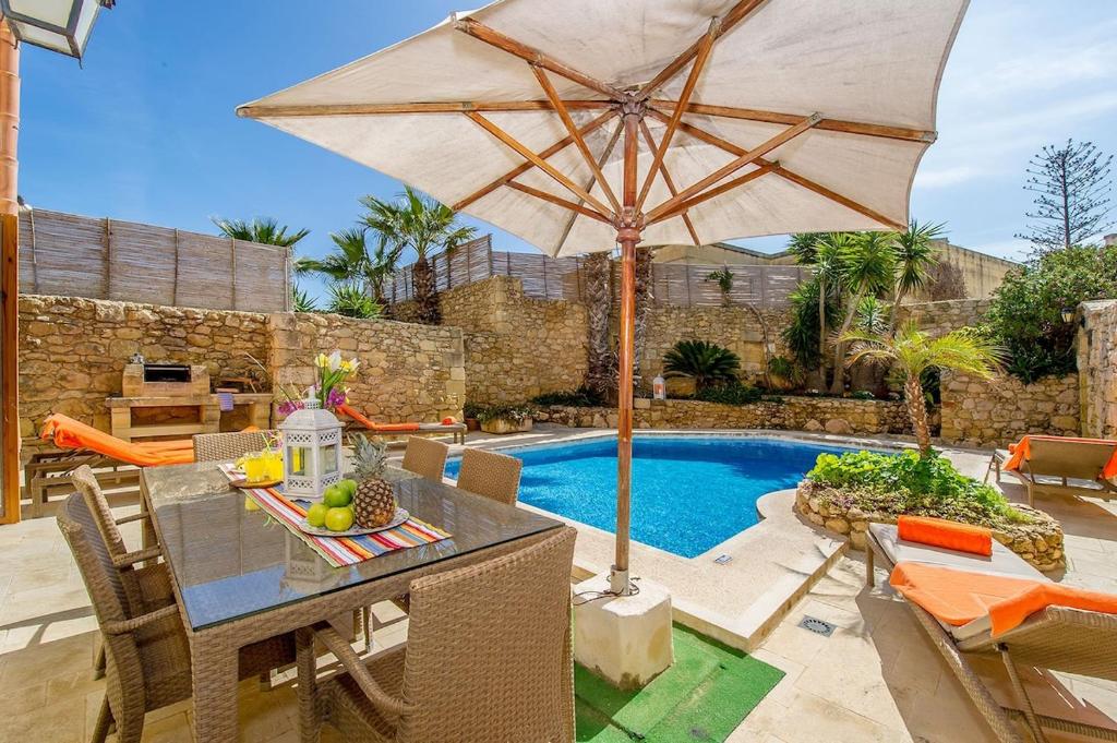 a table with an umbrella next to a swimming pool at Djar ta Menzja 2 Holiday Home in Sannat