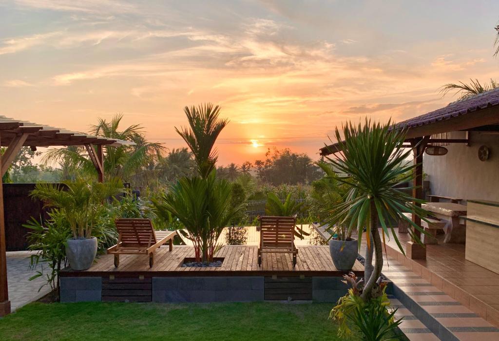 a patio with chairs and palm trees at sunset at Gama’s Villa in Tabanan