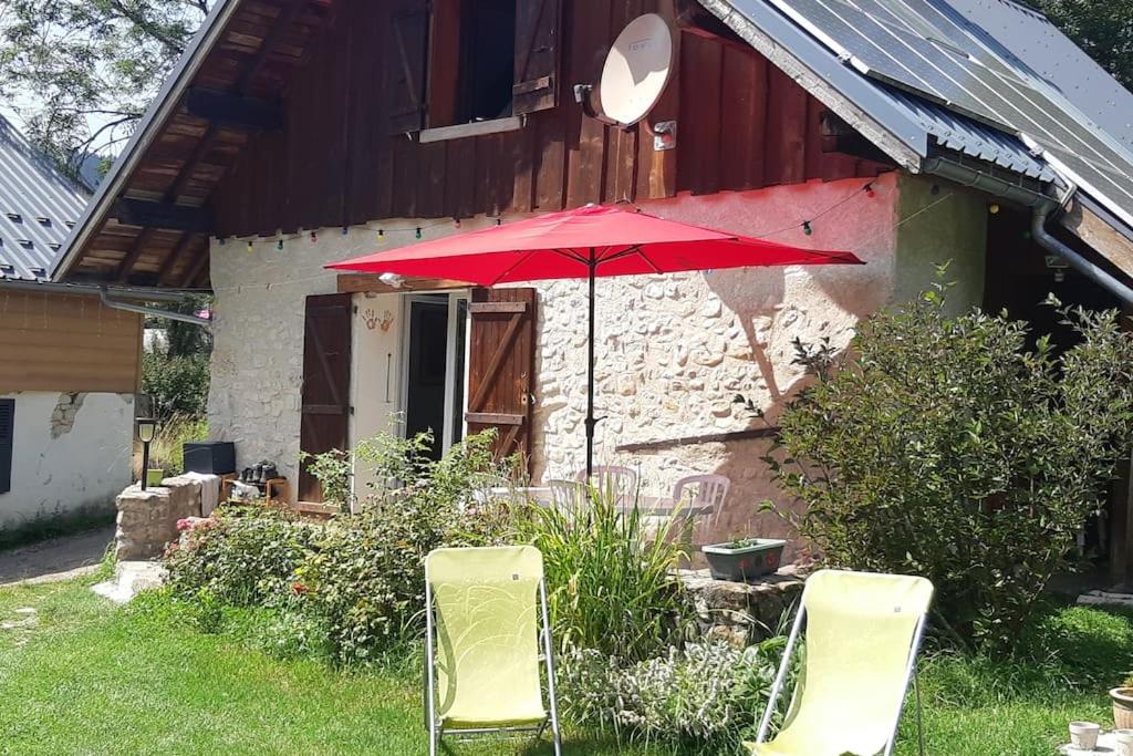 einen roten Regenschirm und zwei Stühle vor einem Haus in der Unterkunft Gite combes soleil calme et nature in Le Sappey-en-Chartreuse