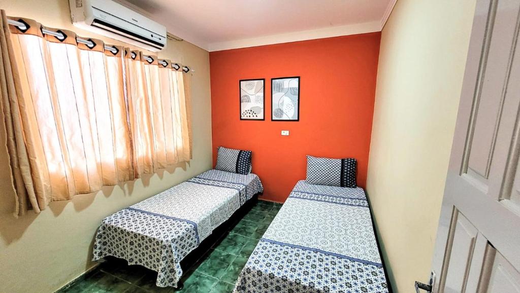 2 Betten in einem Zimmer mit orangefarbener Wand in der Unterkunft House Maraca in Ipojuca