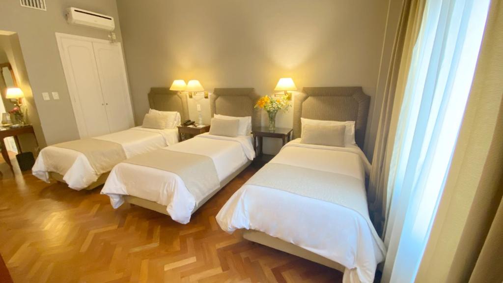 um quarto com três camas com lençóis brancos em Lafayette Hotel em Buenos Aires