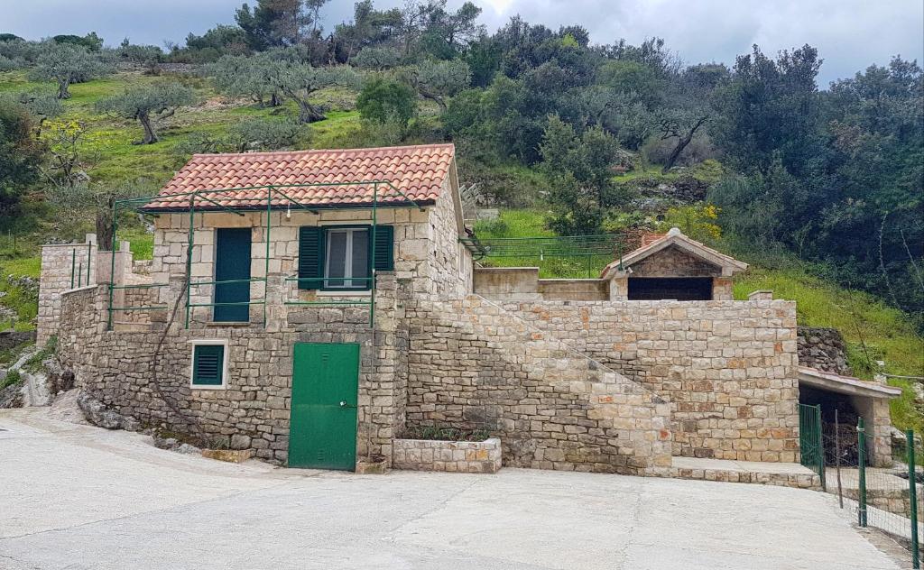 een stenen gebouw met een groene deur en een heuvel bij Secluded holiday house Postira, Brac - 17571 in Postira