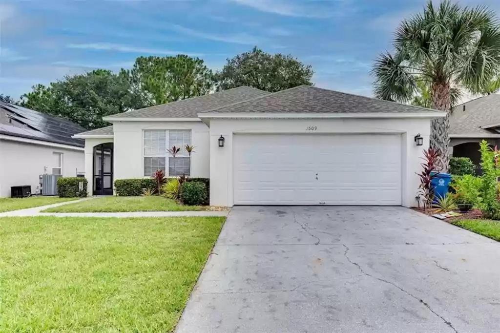 a house with a white garage and a palm tree at Lovely Home in Southern Dunes Golf & Country Club Gated Community in Haines City