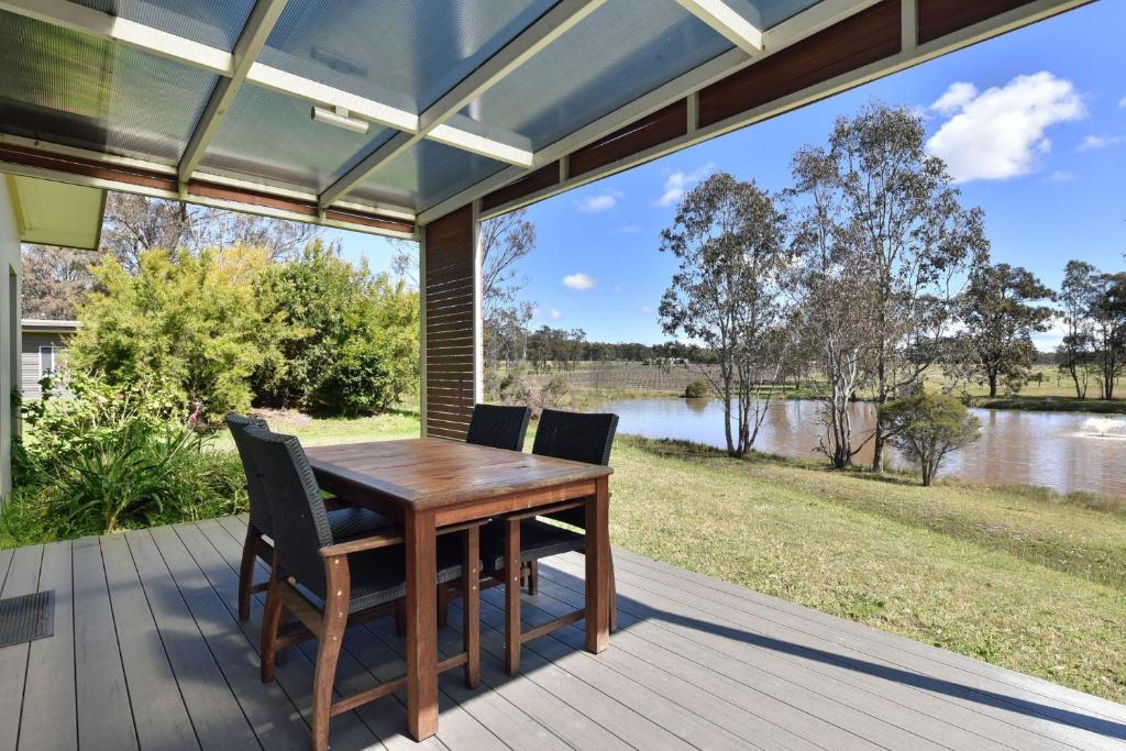 a wooden table and chairs on a porch with a view of a lake at Ironbark Hill Villa 3 Saperavi in Pokolbin