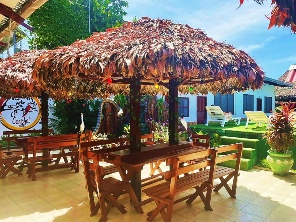 un grupo de mesas de madera con una sombrilla grande en El Curichal Hostel, en Rurrenabaque