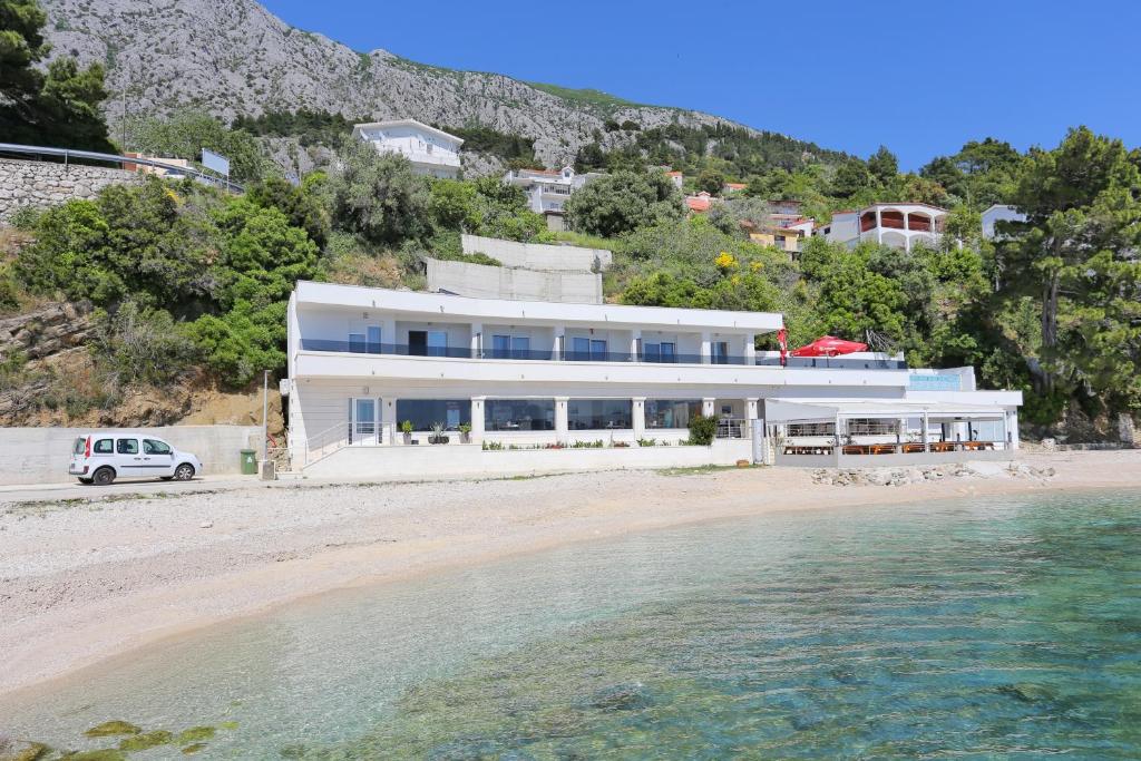 a white house on a beach with the water at Family friendly apartments with a swimming pool Zivogosce - Porat, Makarska - 18150 in Živogošće