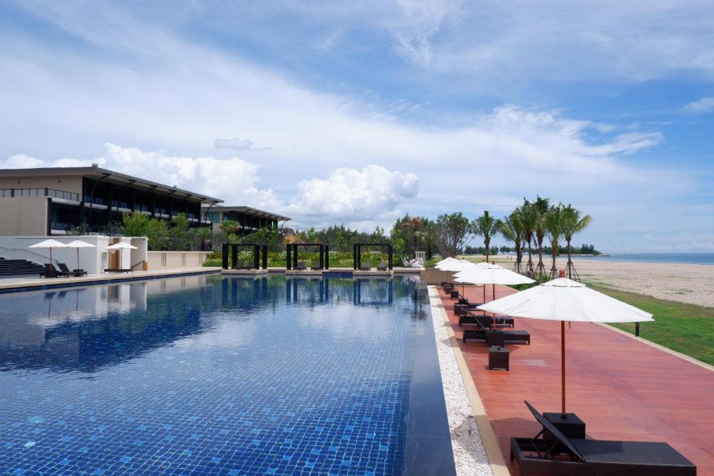 a swimming pool with umbrellas and the ocean at Sea Sand Sun Hua Hin Resort in Phetchaburi