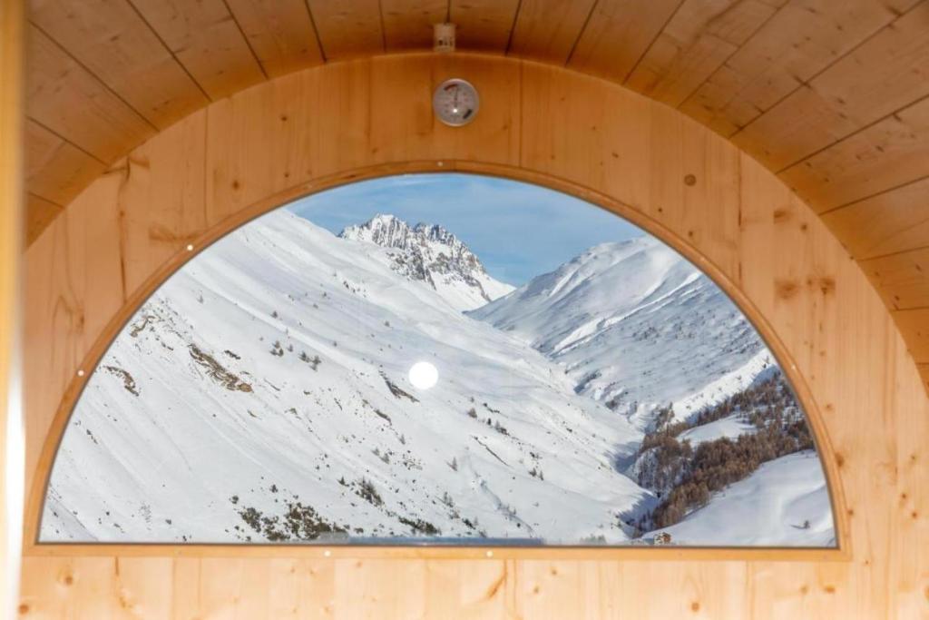 a window in a wooden building with a snow covered mountain at BAITA NOEMI in Livigno
