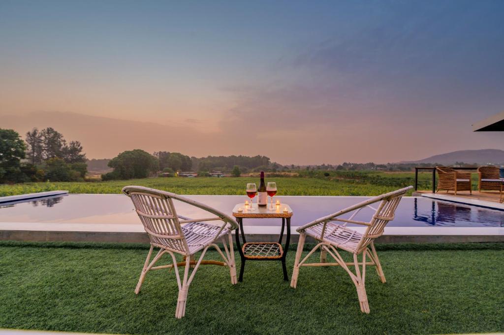 duas cadeiras e uma mesa com copos de vinho em SaffronStays Onellaa, Nashik - infinity pool villa surrounded by a vineyard em Nashik