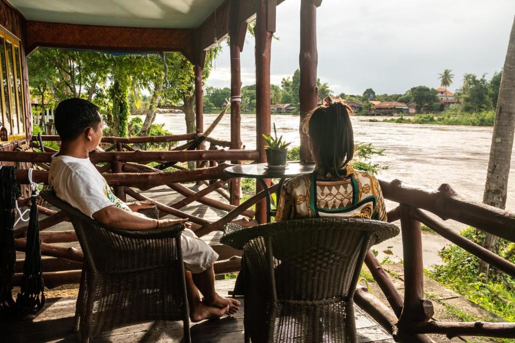a man and a woman sitting at a table near a river at Nongsak Riverside Guesthouse & Nongsak Guesthouse in Ban Khon