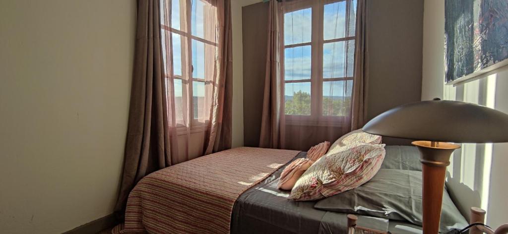 a bedroom with a bed with a lamp and windows at L'Atelier B&B - Esprit bohème, la nature en ville in Carcassonne