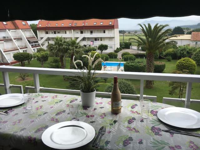 una mesa con platos y una botella de vino en el balcón en Duplex con piscina muy cerca de la playa, en Santiuste