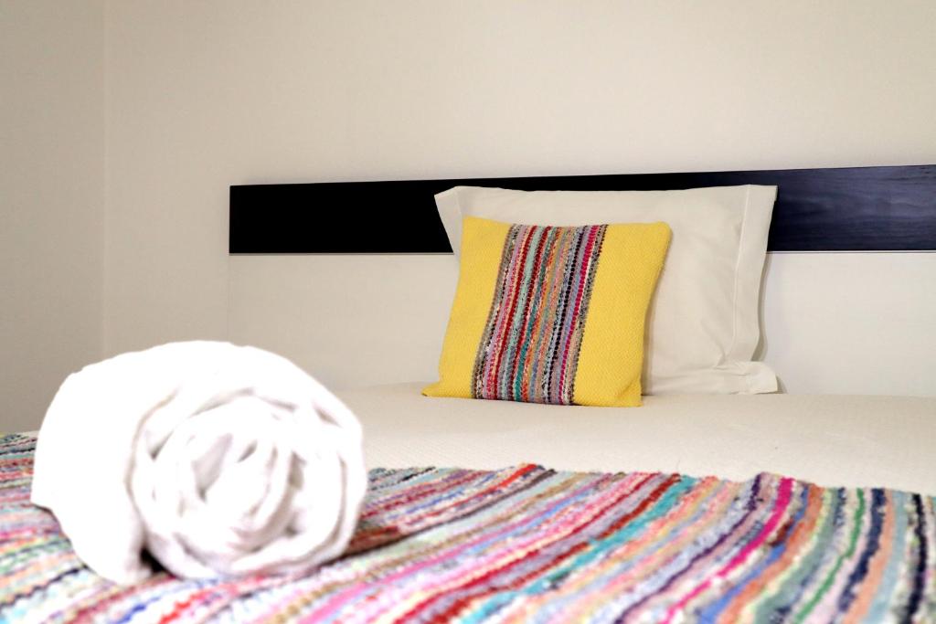 a bed with a colorful blanket and a yellow pillow at Breathe In in Zambujeira do Mar