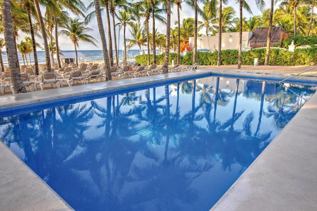 einen Pool neben einem Strand mit Palmen in der Unterkunft Riu Lupita - All Inclusive in Playa del Carmen