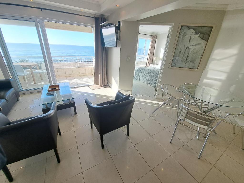 a living room with a table and chairs and a view of the ocean at 3 Bedroom Sea Facing Family Apartment Cape Town Moullie Point in Cape Town