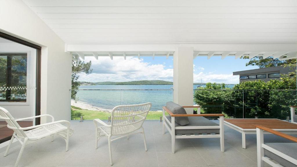 a porch with chairs and a table and a view of the water at Baywatch - Beachfront Bliss Executive Home in Soldiers Point