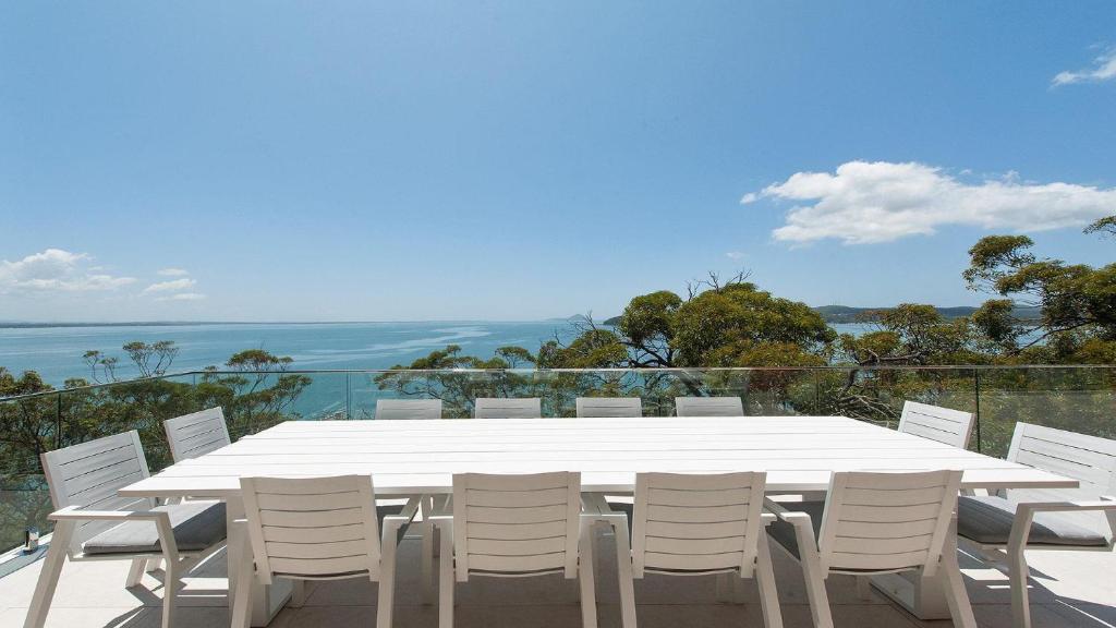 a white dining table and white chairs on a balcony at The Family Entertainer - with sweeping water views in Salamander Bay