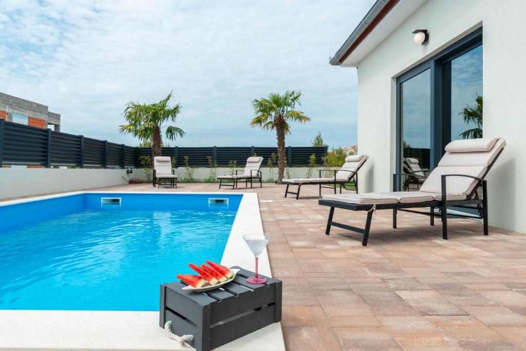 eine Terrasse mit einem Pool, Stühlen und einem Tisch in der Unterkunft Luxury villa with a swimming pool Vrsi - Mulo, Zadar - 19140 in Vrsi