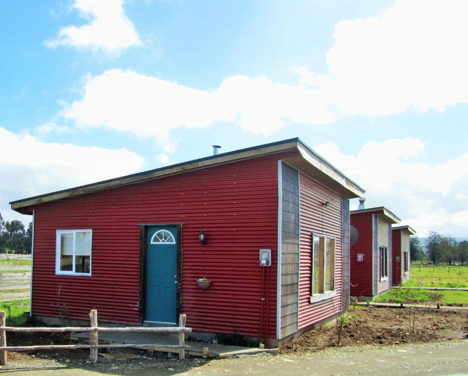 een rood huis met een blauwe deur naast een veld bij Cabañas Juan José in Castro