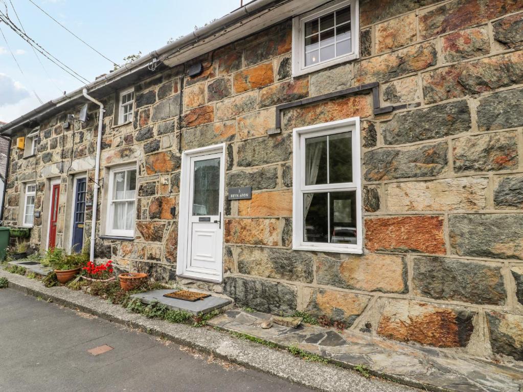 a stone building with a white door and windows at Bryn Afon in Caernarfon