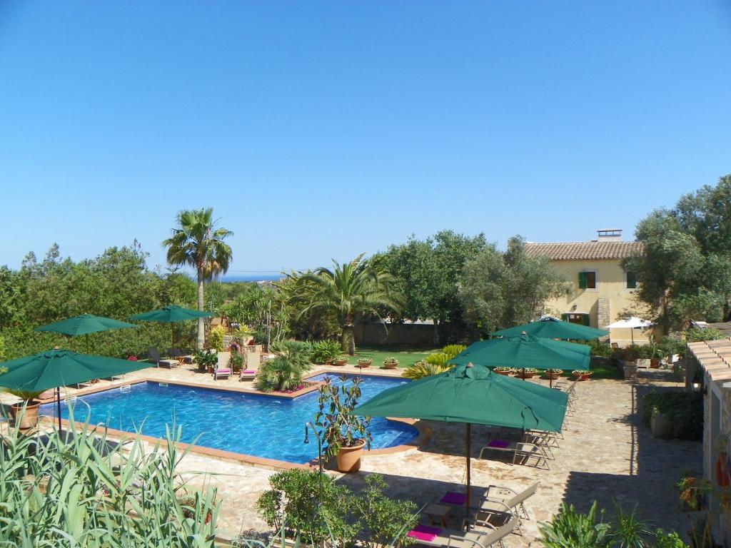 una piscina con sombrillas verdes, mesas y sillas en Agroturisme Can Bessol en S'Horta