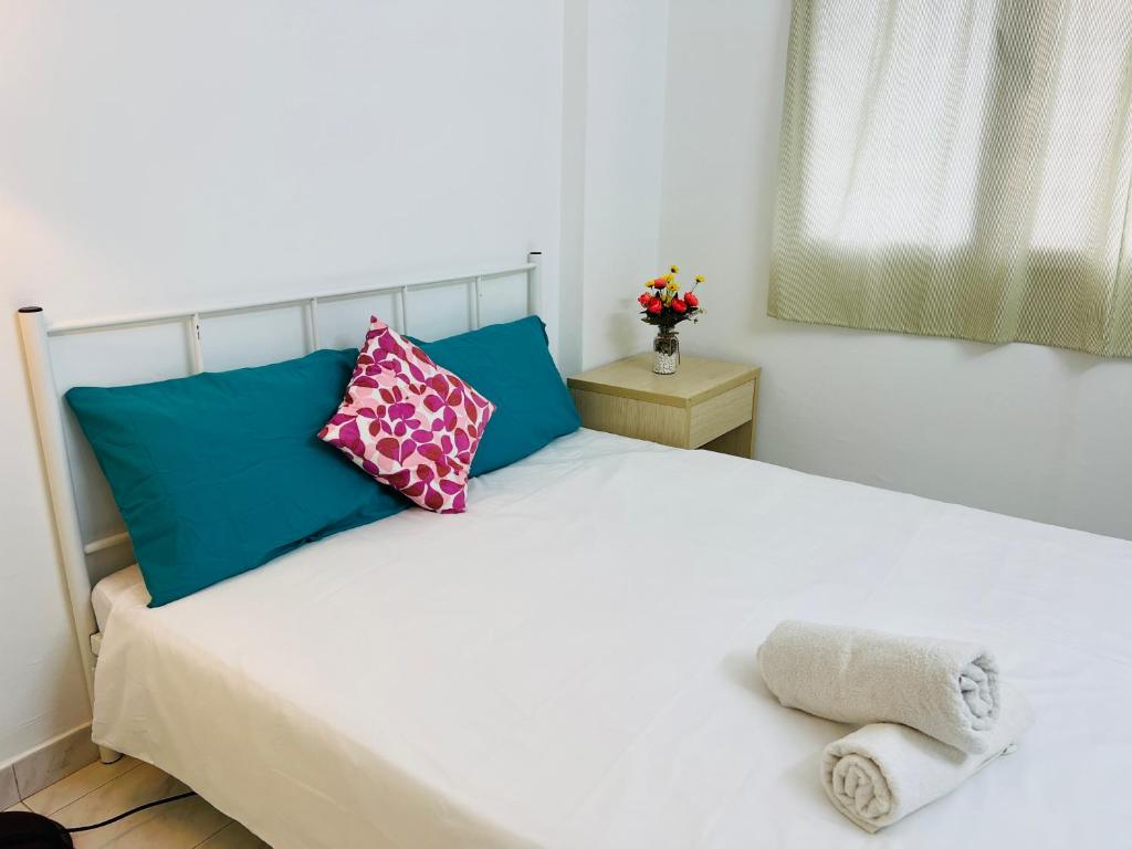 ein Schlafzimmer mit einem weißen Bett mit blauen und rosa Kissen in der Unterkunft KL Rinas Best Homestay at Bukit Bintang City Center in Kuala Lumpur