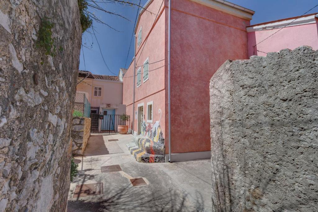 a red building with a wall next to a street at Apartments by the sea Veli Losinj, Losinj - 19620 in Veli Lošinj
