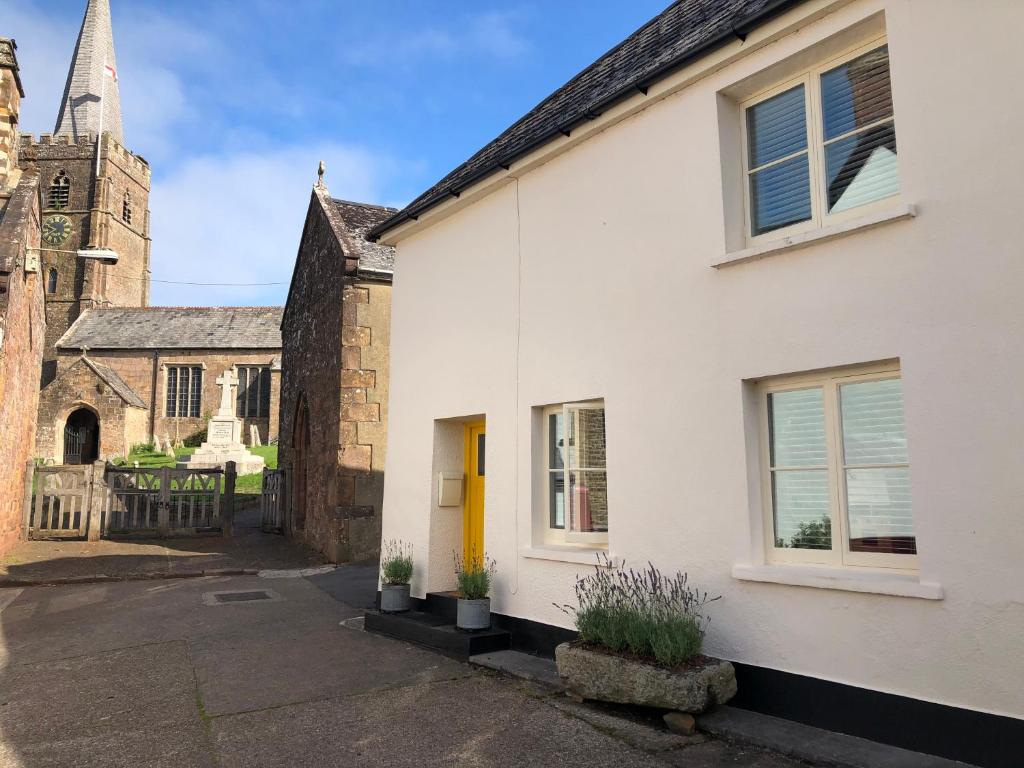 a white building with a yellow door and a church at Church View - c. 1750 cosy character cob cottage. in Hatherleigh