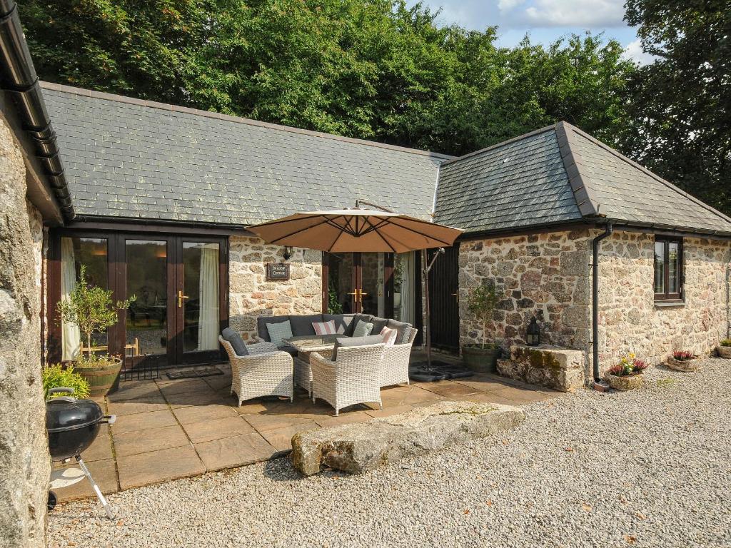 a patio with a table and chairs and an umbrella at Lydgate House Cottage in Yelverton