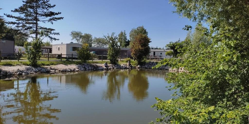 a river with trees and buildings in the background at Camping de la Plage in Marck