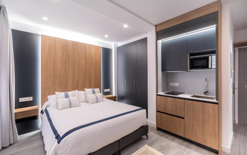 a bedroom with a white bed and a kitchen at Jerusalén Suites Alicante in Alicante