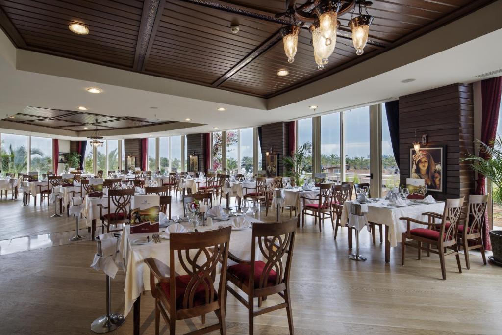 a restaurant with white tables and chairs and windows at Liberty Hotels Lara in Lara