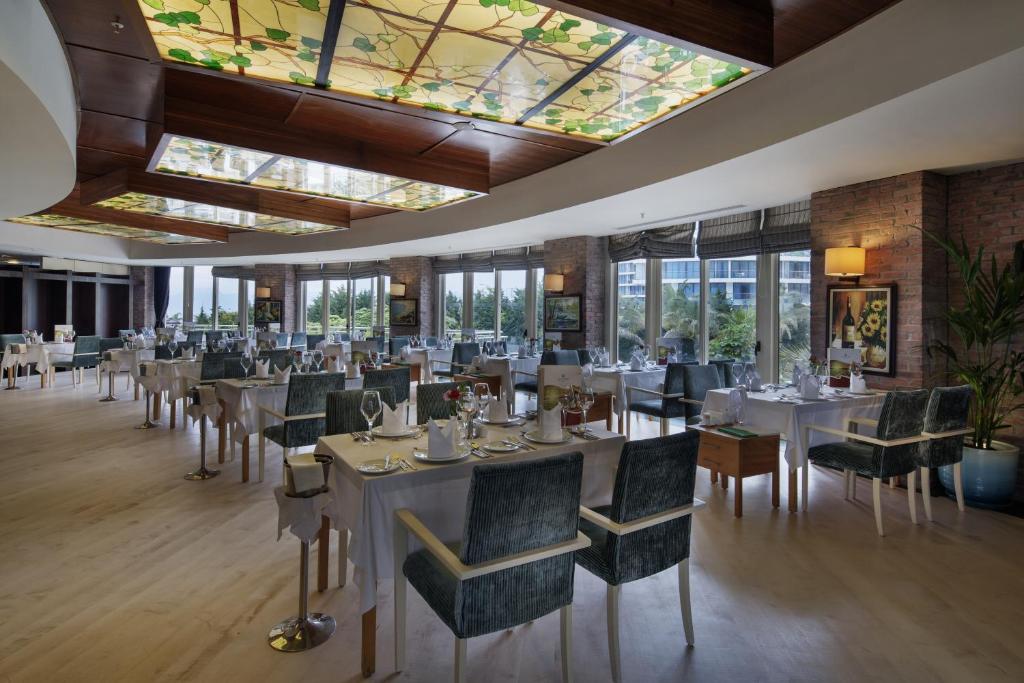 a restaurant with white tables and chairs and windows at Liberty Hotels Lara in Lara