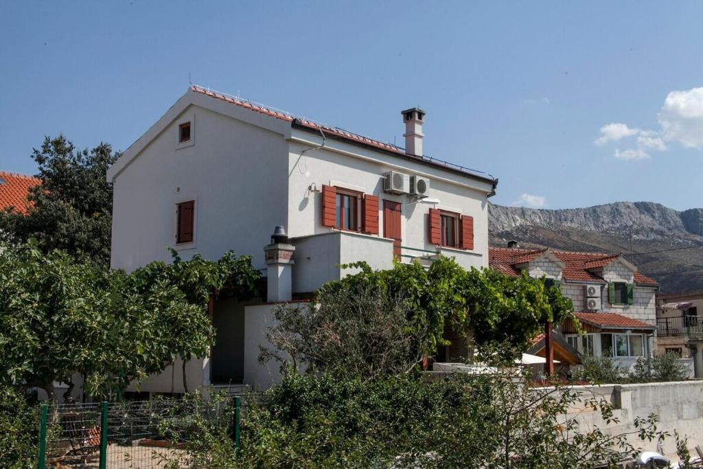 ein weißes Haus mit roten Fensterläden und Bäumen in der Unterkunft Holiday house with a parking space Mravince, Split - 19827 in Solin