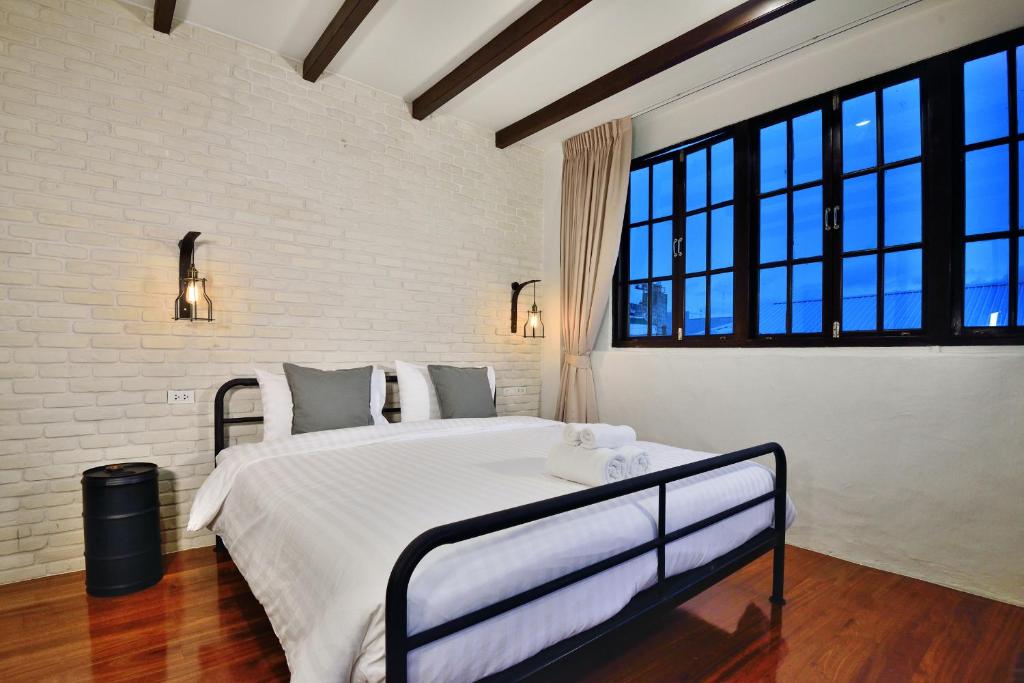 a bedroom with a bed with white sheets and windows at The Rommanee Classic Guesthouse in Phuket