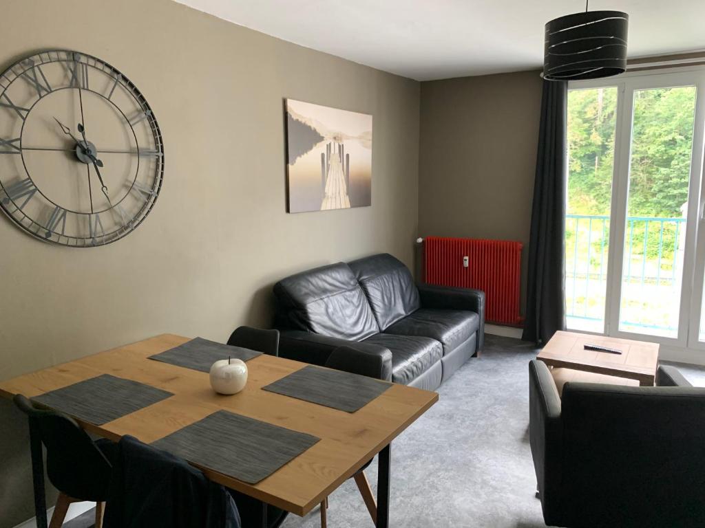 a living room with a table and a clock on the wall at Appartement tout confort dans une résidence calme in Givet